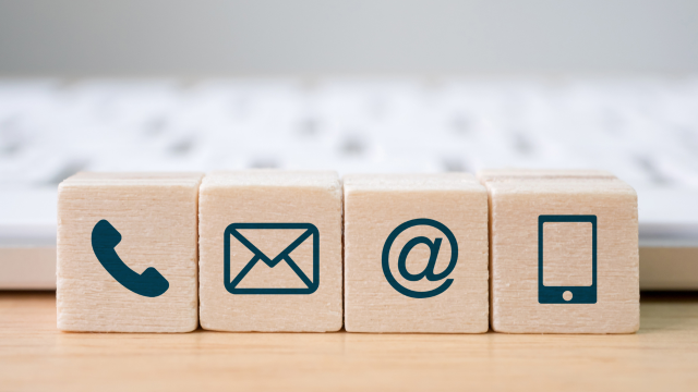 Four stacked wooden blocks showing blue icons for phone, envelope, email symbol, and smartphone, representing different contact methods.