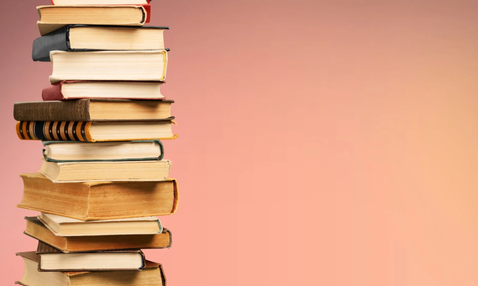 A tall stack of assorted hardcover and paperback books arranged unevenly against a plain gradient background transitioning from light pink to peach.